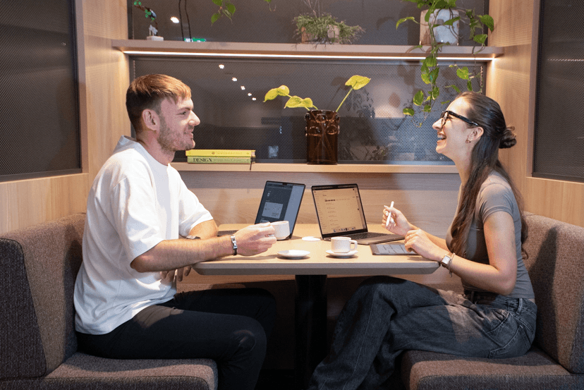 Lena and Ben at the table with their MacBooks and coffee.